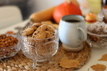 Lit candles, cookies, chocolate, nuts, tea, wine, pumpkins, books, reading glasses and autumn leaves on the table. Autumnal hygge at home. Selective focus.