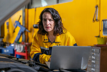 female mechanic or engineer in workwear using laptop checking car engine to diagnostic and repair in auto services