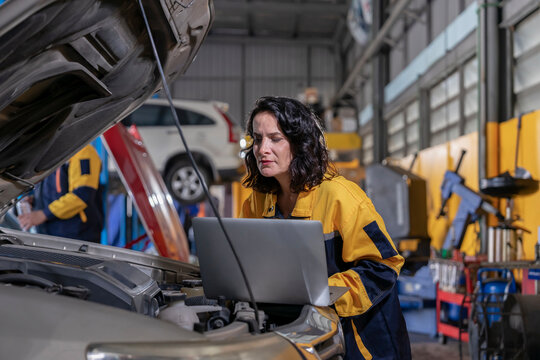 female mechanic or engineer in workwear using laptop checking car engine to diagnostic and repair in auto services - Powered by Adobe