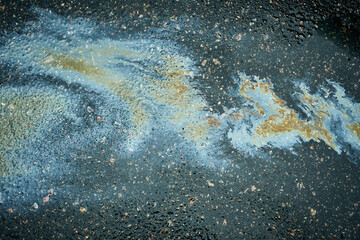 Oil puddle creating colorful iridescent abstract pattern on wet dark asphalt.