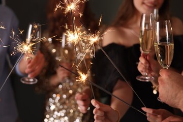 Friends celebrating New Year with sparklers and wine glasses indoors, closeup
