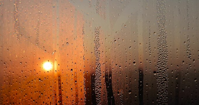 water from condensation on the window glass at sunset, wet glass with lots of water droplets on the background of an orange sky out of focus at sunset