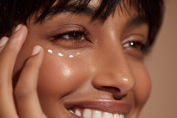 Woman applying white cream dots under eye for skincare routine in a warm light studio