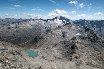 View from Ankogel towards Hochalmspitze (3,360 m) with rugged alpine peaks, rocky ridges, and turquoise mountain lake under a clear blue sky in the Austrian Alps.