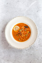 Rich soup with smoked meats, sausages, lemon, and olives, viewed from above on a gray background