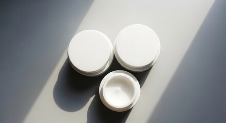 Three white cosmetic cream jars on grey background with strong shadows