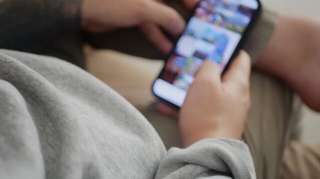Man using his smartphone to scroll through an Instagram feed, browsing posts and videos. 4K UHD.