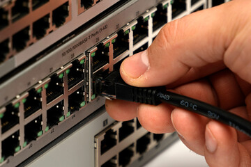 Close-up of hand plugging Ethernet cable into network switch port, symbolizing digital connectivity, data transfer, and essential infrastructure of modern communication.