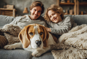 Cozy family tea time. Father, mother and son at the home living room. Boy lying in comfortable sofa and stroking their beagle dog and smiling. Peaceful family moments concept image.