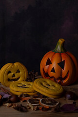Close-up of a pumpkin with eyes, Halloween cookies, leaves, and nuts, vertically with copy space