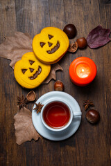 Top view of a cup of tea with Halloween cookies, an orange candle, leaves, and nuts, vertically with copy space.