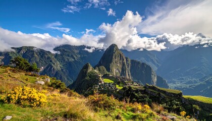 Obraz premium Majestic mountain landscape featuring a lush green foreground with yellow wildflowers under a vibrant blue sky filled with fluffy white clouds; ancient stone structures are nestled amongst the peaks.