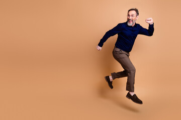 Mature professional man in formal attire showcasing energetic pose against beige background, expressing enthusiasm and confidence