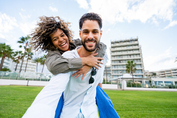 Happy diverse couple enjoying piggyback ride in a summer park