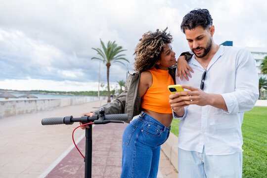 Couple using smartphone next to electric scooter by sea - Powered by Adobe