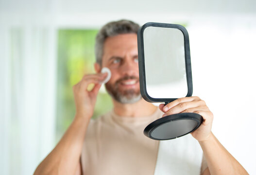 Latin male practicing grooming with dermatology-approved skincare products. Millennial man doing a beauty facial routine with natural cosmetics. Attractive male applying moisturizer. - Powered by Adobe