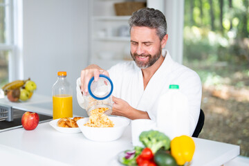 Happy man eating morning breakfast. Healthy food in kitchen for aged mature man. Portrait of senior man at kitchen and eat lunch. 50s man eating breakfast in cozy kitchen at home.