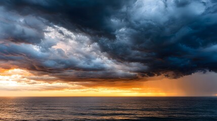 Obraz premium Over the vast ocean, a dramatic sky showcases billowing, dark clouds during a fiery sunset. The horizon is bathed in vibrant orange and golden light, creating a stunning display of natural beauty.