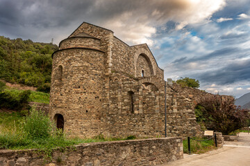 The ancient Romanesque architecture of the historic Sant Serni de Tavèrnoles monastery under a dramatic, stormy sky in the Catalan Pyrenees