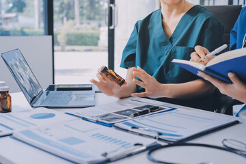 Two doctors and a female nurse meet at a table in the hospital, collaborating on medical tasks using laptops and computers