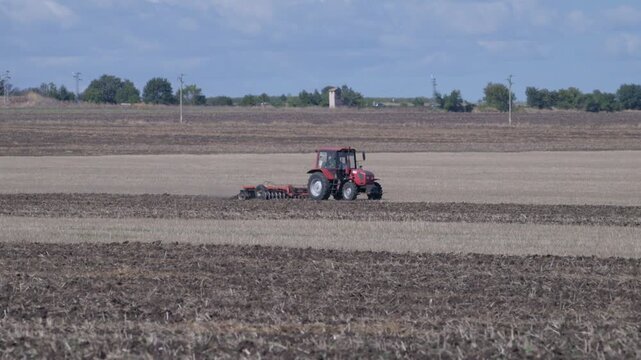 Red tractor plowing a rural field under a partly cloudy sky during autumntime agricultural work.	
