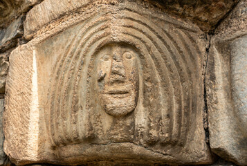 Close-up of a weathered stone capital from the Romanesque church of Sant Lliser d'Al&oacute;s d'Isil, carved with a primitive, stylized human face. Catalonia, Spain.
