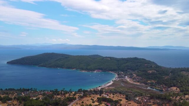 Drone footage captures the stunning panoramic aerial view of Akb&uuml;k Bay within the G&ouml;kova Gulf, Muğla, Turkey. This beautiful Mediterranean coastal landscape features crystal clear turquoise waters, a 