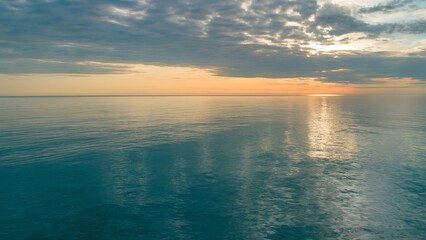 Obraz premium Ocean Sunset with Reflective Water and Cloudy Sky horizon.