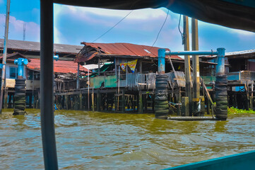Stilt houses on the Chao Phraya River in Bangkok, Thailand. Contrast of traditional dwellings and a modern skyscraper.