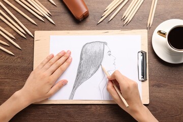 Woman drawing portrait sketch at wooden table, top view