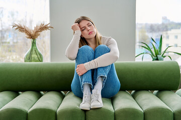 Unhappy upset young woman sitting on sofa at home, face close-up