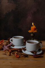 Close-up of two cups of tea on a wooden table with nuts, leaves, and a lit candle, vertically with copy space