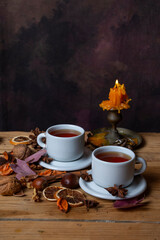 Top view of two cups of tea on a wooden table with nuts, leaves, and a lit candle, vertically with copy space