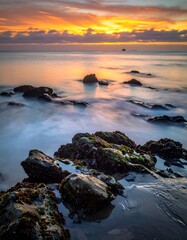 Naklejka premium Coastal sunset, tranquil rocks, soft waves