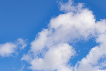 Bright blue sky with fluffy white clouds. Natural background with soft cloud shapes illuminated by sunlight. Perfect for weather, nature, and landscape themes.