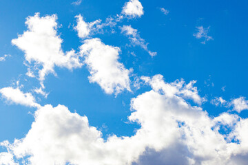 Obraz premium Bright blue sky with fluffy white clouds. Natural background with soft cloud shapes illuminated by sunlight. Perfect for weather, nature, and landscape themes.