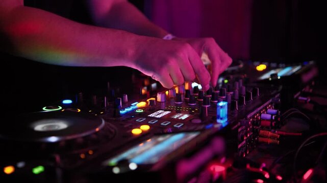Professional disc jockey performing and mixing music on a sound controller during a live set at a nightclub party, with hands adjusting faders and knobs on the illuminated audio equipment