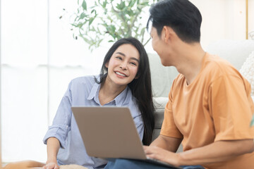 Happy couple relaxing at home with laptop and pet dog in cozy living room. Concept of modern lifestyle, remote work, online shopping, love, technology, and family comfort in bright natural light.