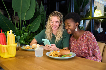 Diverse women friends smiling using smartphone during lunch