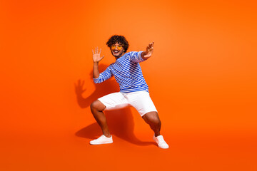 Young stylish man making fun poses in a striped shirt against bright orange background, embodying joy and energy
