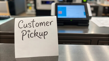 Omnichannel retail enhances customer experience. Customer pickup sign displayed at a counter with a digital screen in the background.