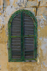 Weathered Green Arch Window Shutter On Crumbling Yellow Wall Exuding Rustic Mediterranean Charm