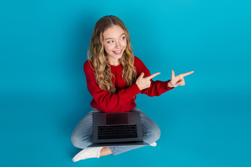 Adorable young girl in a red sweater enjoying leisure time with laptop on blue background