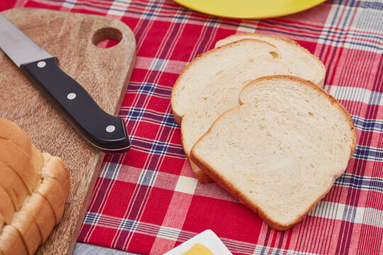 Three slices of Jamaican hard dough bread on a Jamaican bandana with a yellow plate, cutting board, knife and a stick of butter