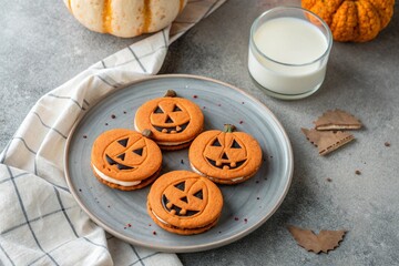Halloween pumpkin cookies with sweet cream filling on a gray plate with milk on a concrete background. 