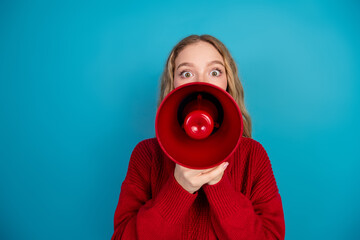 Fototapeta premium Cheerful young woman in casual attire shouting excitedly through a red megaphone against a vibrant blue background