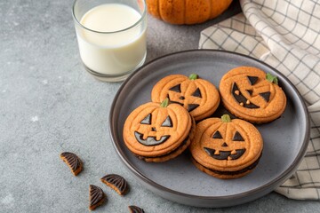 Halloween pumpkin cookies with sweet cream filling on a gray plate with milk on a concrete background. 