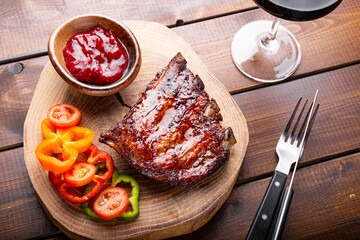 BBQ pork ribs from pork tenderloin with vegetables, cranberry sauce and a glass of red wine on board and wooden background