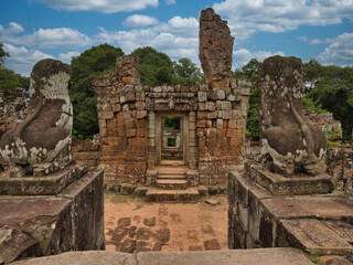 Brahma's Temple in Cambodia - Crumbling temple ruins of Brahma, with large stones in the foreground and a dramatic blue sky with clouds.