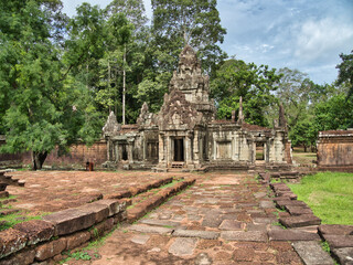 Preah Pithu Temple - A weathered, ancient temple in the Preah Pithu complex, with a worn stone pathway leading to the main structure, surrounded by jungle.